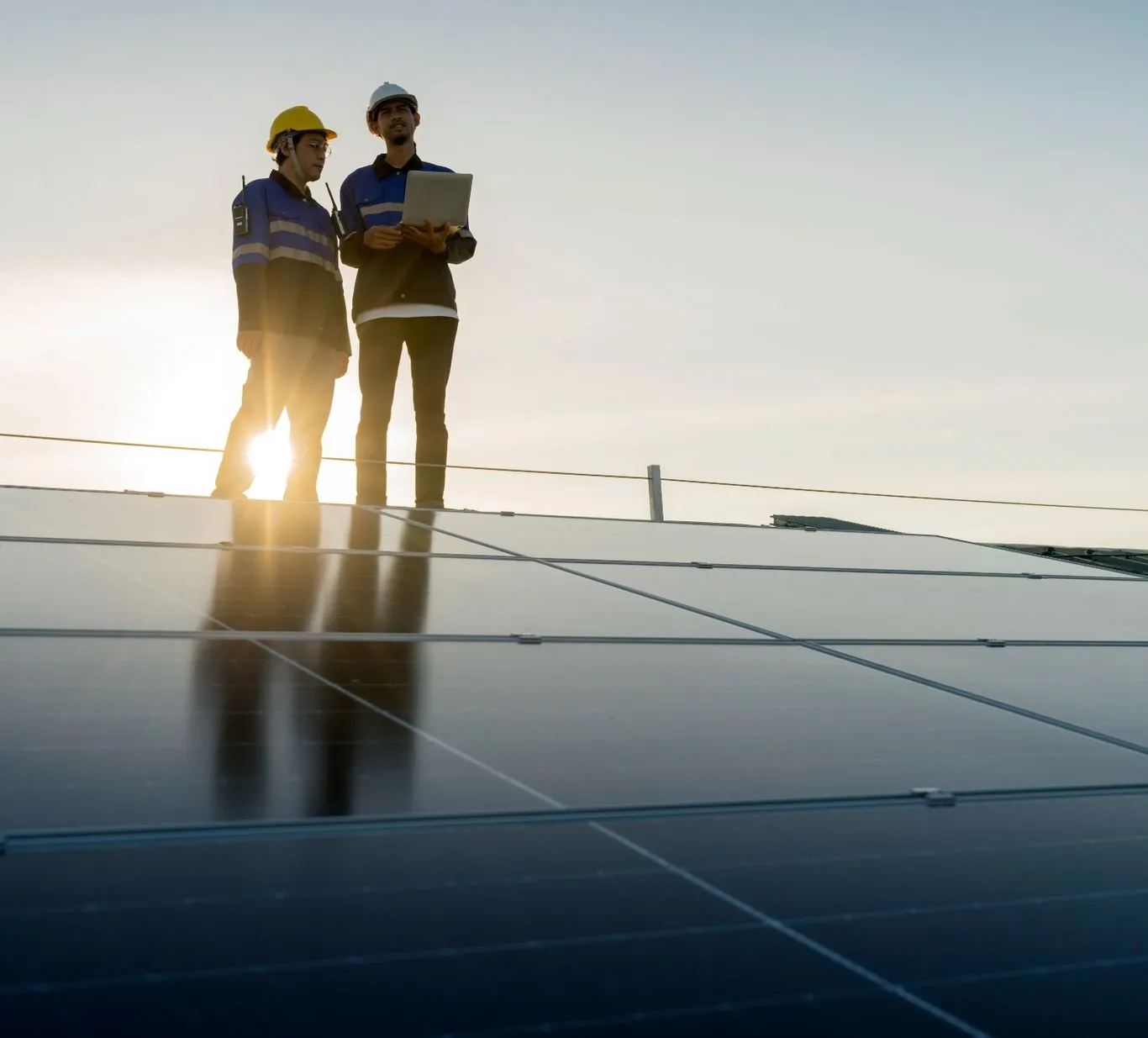 Zwei Monteure stehen bei tief stehender Sonne auf einer großen Solaranlage