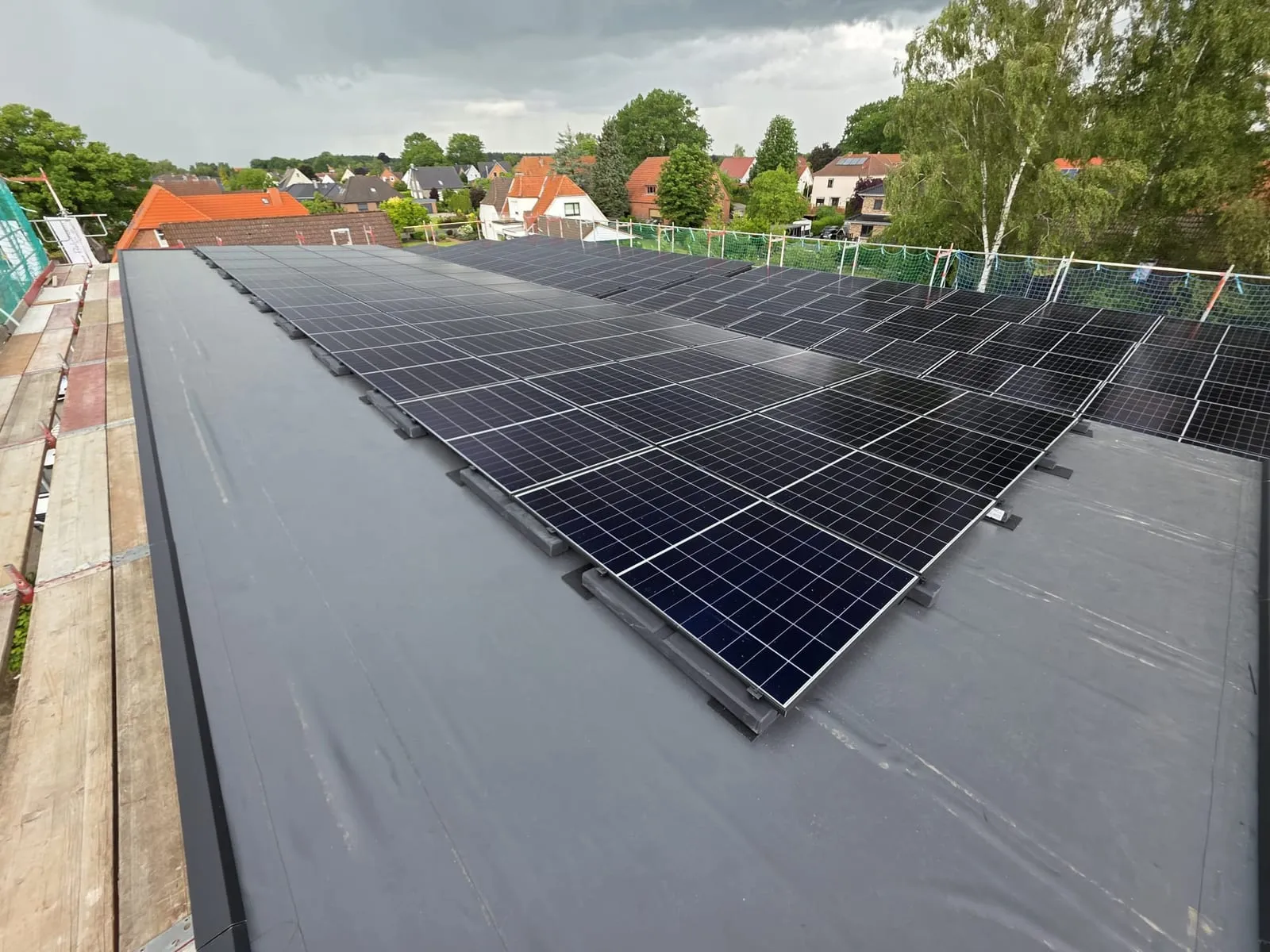 Fertig belegtes Flachdach mit schwarzen Photovoltaikmodulen, im Hintergrund ein Wohngebiet